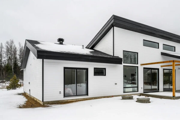 Maison moderne enneigée, grandes fenêtres, toit pentu.